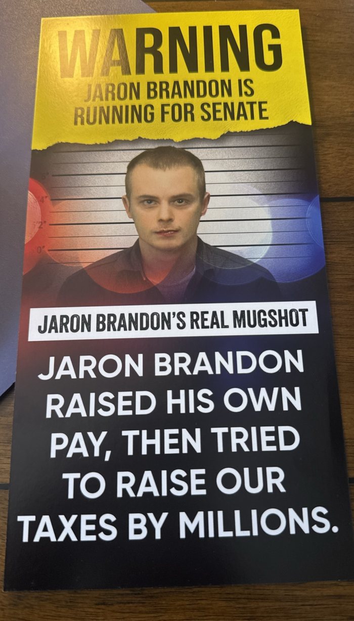Card: “Jaron Brandon’s real mugshot. Jaron Brandon raised his own pay, then tried to raise our taxes by millions.”